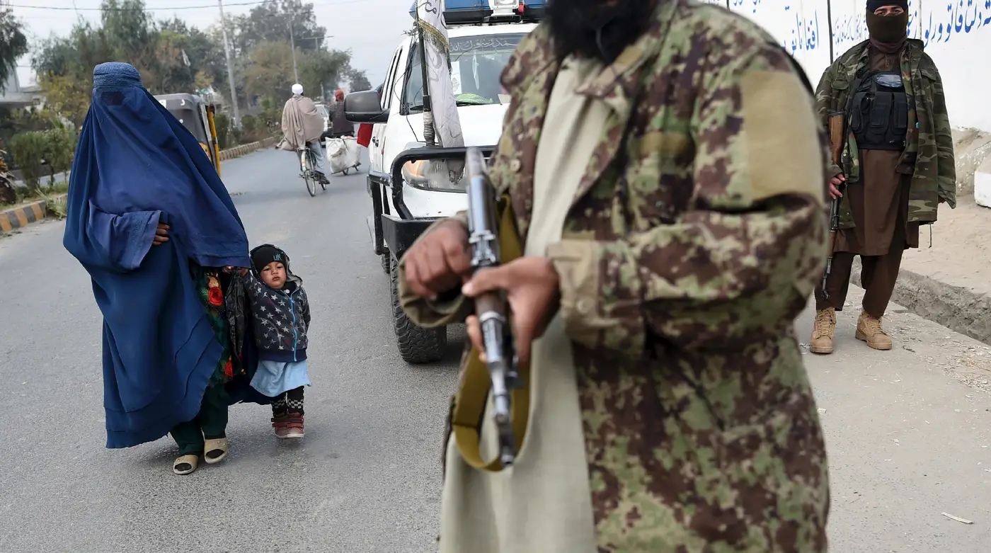 زنی در حال عبور از پهلوی جنگ‌جویان طالبان. عکس تزئینی است. منبع:https://www.laprovence.com